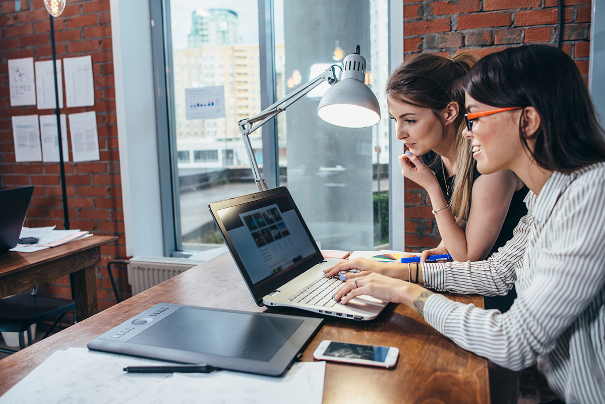 Two women studying laptop screen in office